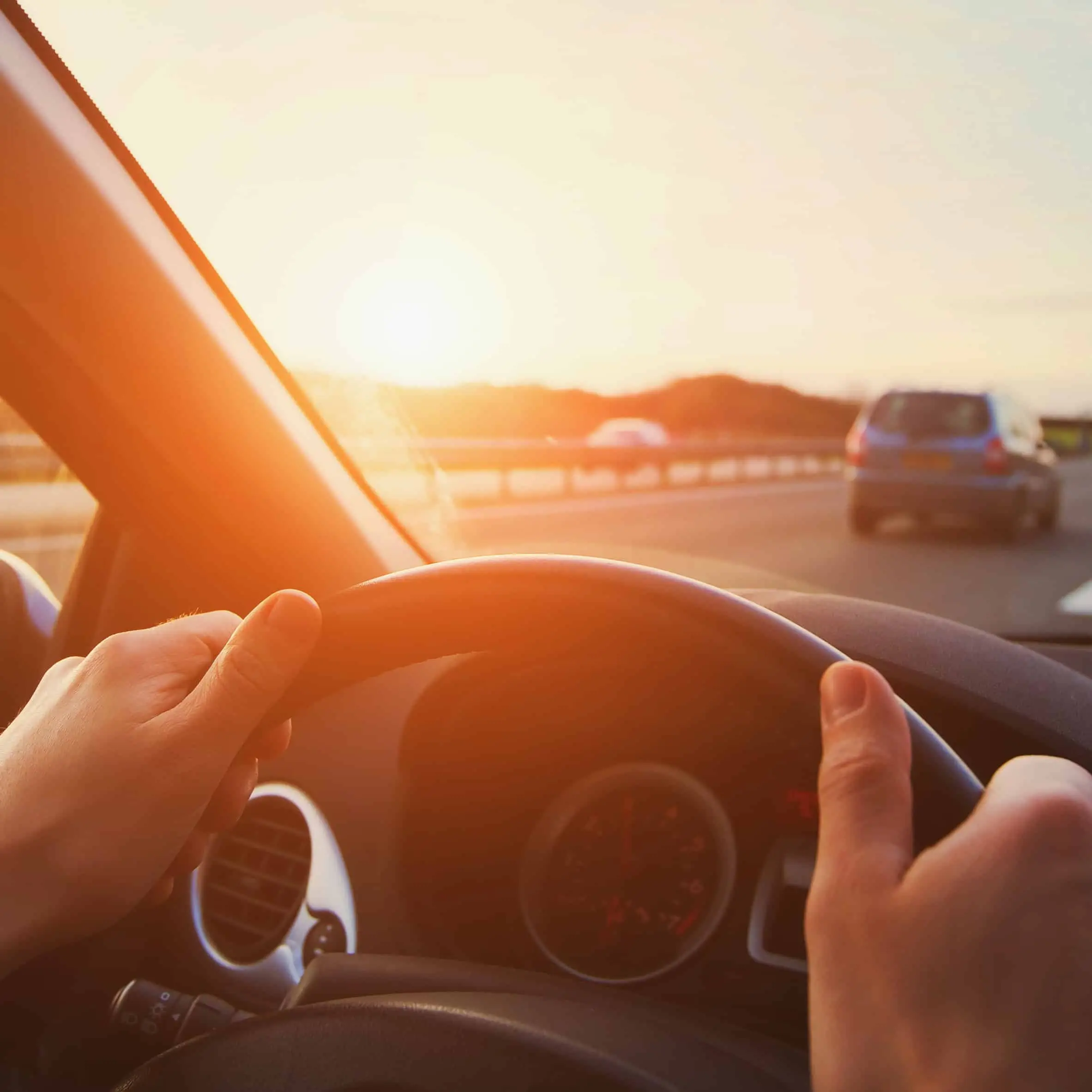 Mains sur le volant d'une voiture roulant sur une autoroute au soleil.
