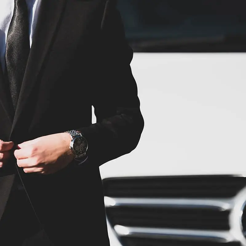 Homme en costume noir avec une montre devant une voiture